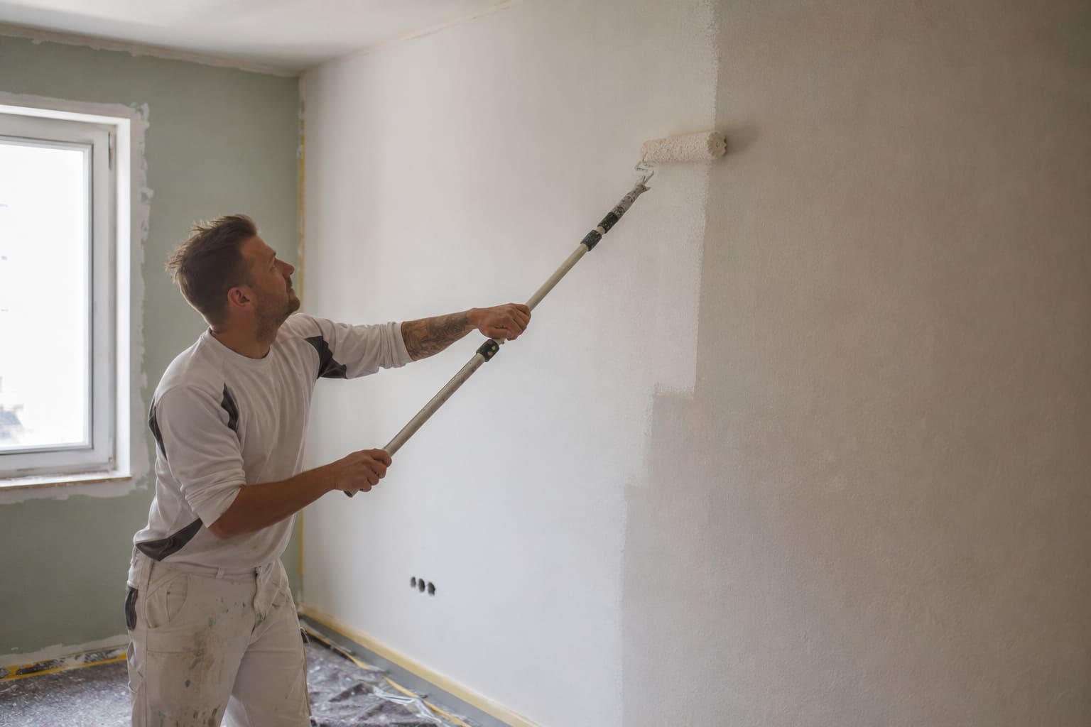 Maler rollt mit der Teleskoprolle eine große Wandfläche
